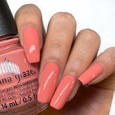 A Medium skin tone woman's hand nail with a glimpse of pink corally creme nail polish bottle from China Glaze